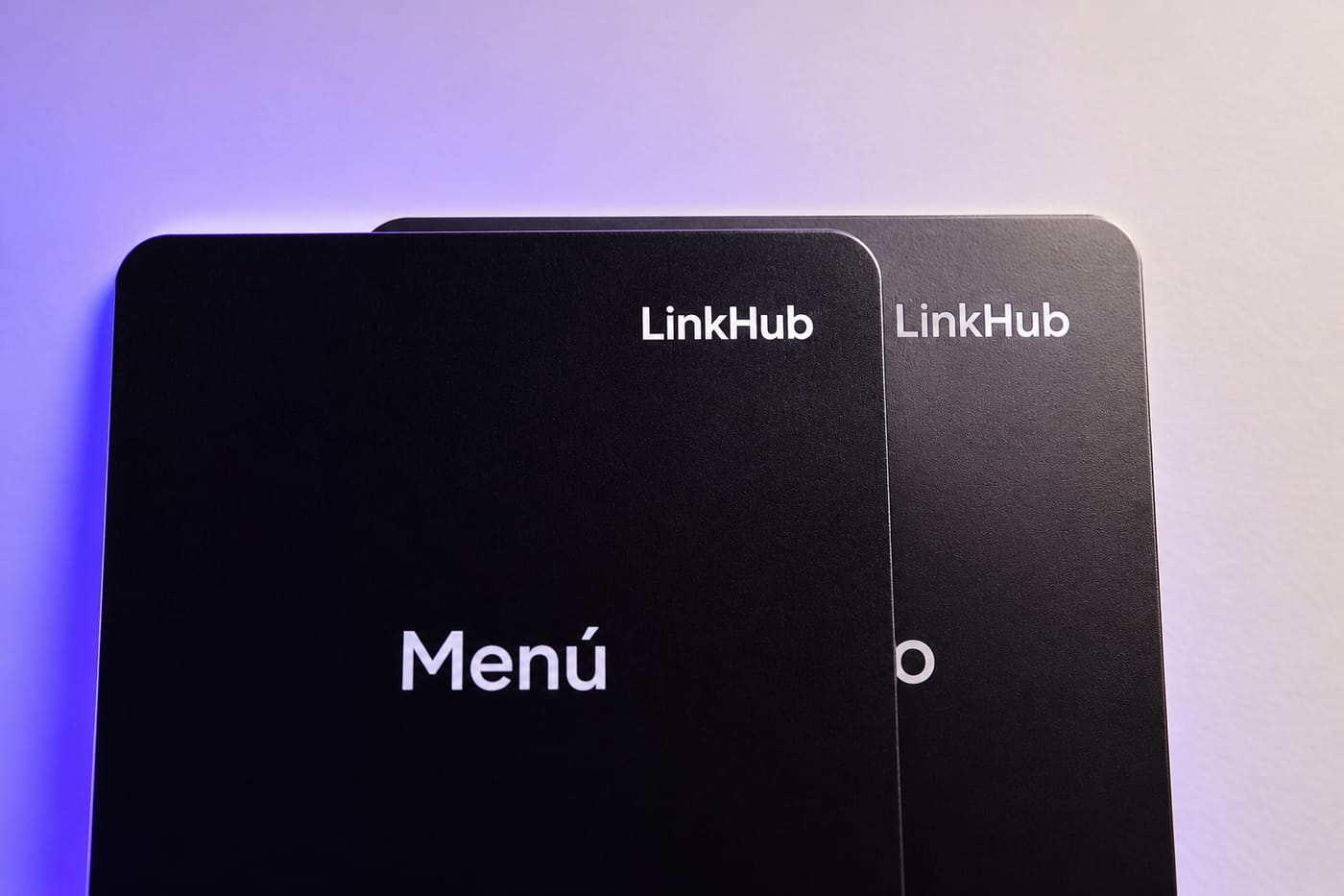 Dos placas negras superpuestas sobre un fondo claro con luz violeta: la de adelante dice «Menú» y de la de atrás se ven el logo de LinkHub y el final de su título