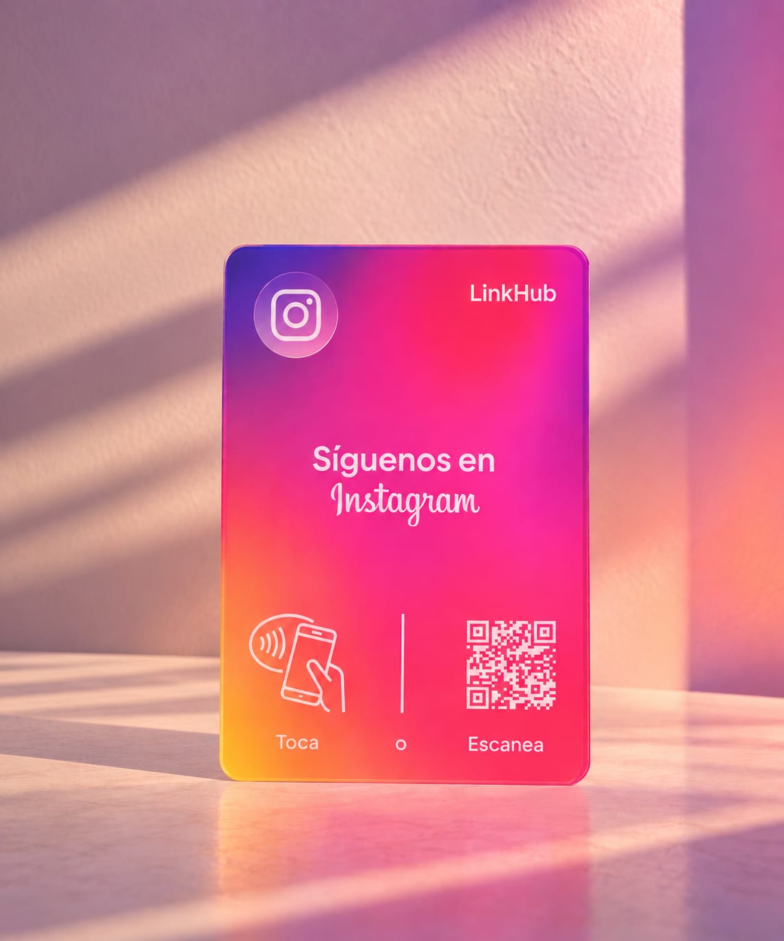 Placa vertical de LinkHub en degradado morado, rosado y naranja con el logo de Instagram y el texto «Síguenos en Instagram», sobre una mesa clara con sombras de ventana